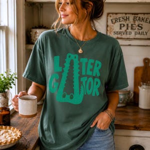 Blue Spruce Comfort Colors graphic tee featuring a playful Later Gator alligator illustration forming the letter A in chunky retro green typography.