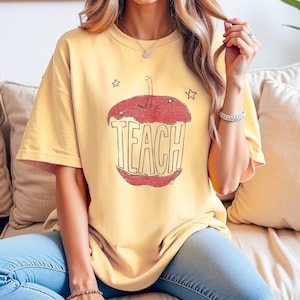 Aesthetic teacher shirt in butter yellow featuring hand drawn apple with TEACH lettering, vintage sketch style teacher tee inspired by Anthropologie