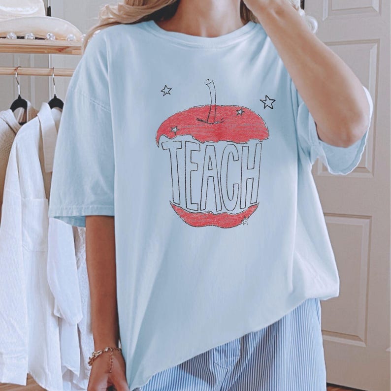 Light blue teacher shirt featuring hand drawn apple illustration and TEACH lettering, relaxed boho teacher tee with Free People inspired aesthetic
