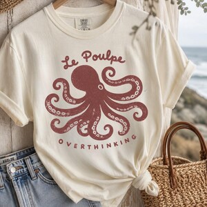 Ivory Comfort Colors octopus graphic shirt flat lay with denim and straw tote.