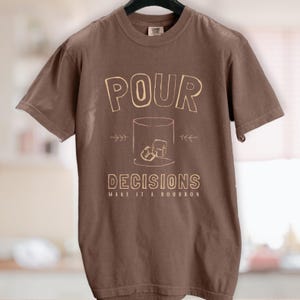 For the bourbon lovers! POUR DECISIONS (make it a bourbon) with a simple distressed line drawing of a whiskey glass with two ice-cubes. Cream graphics on espresso brown.