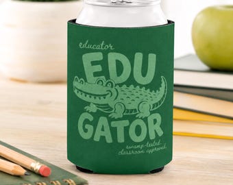 May include: A dark green foam can cooler featuring a light green graphic of an alligator. The text reads "educator EDU GATOR" and "swamp-tested. classroom approved." The cooler is cylindrical and designed to hold a standard beverage can.