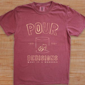 For the bourbon lovers! POUR DECISIONS (make it a bourbon) with a simple distressed line drawing of a whiskey glass with two ice-cubes. Cream graphics on brick COMFORT COLORS.