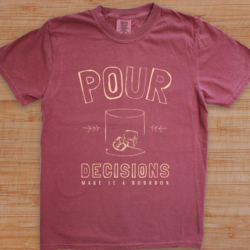 For the bourbon lovers! POUR DECISIONS (make it a bourbon) with a simple distressed line drawing of a whiskey glass with two ice-cubes. Cream graphics on brick COMFORT COLORS.