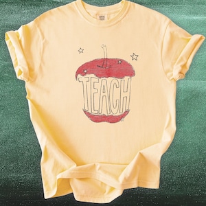 Aesthetic teacher shirt in butter yellow featuring hand drawn apple with TEACH lettering, vintage sketch style teacher tee inspired by Anthropologie