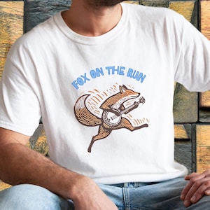 May include: White t-shirt with a graphic of a fox playing a banjo and the text "Fox on the Run".