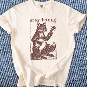 May include: A white ceramic mug with a black handle and the text "But First, Coffee" in a black, handwritten-style font. The mug is on a white surface.