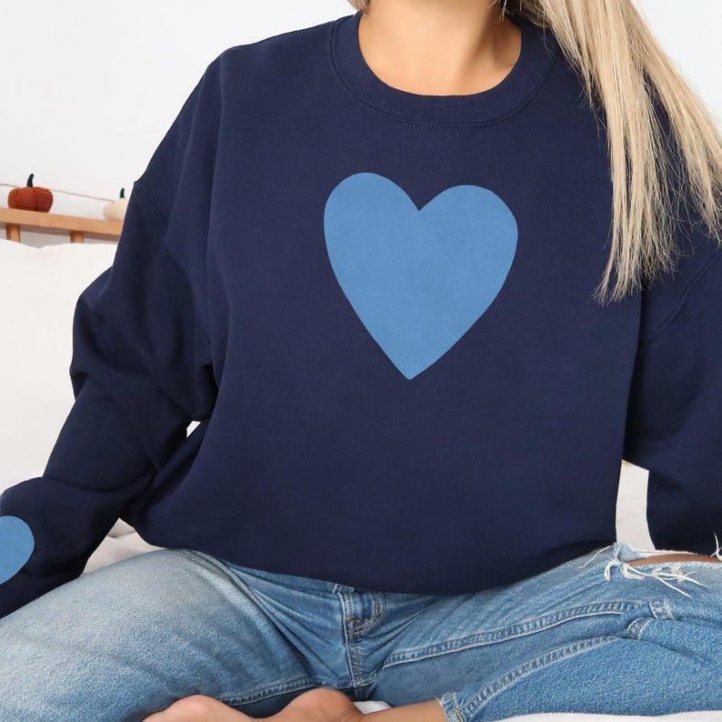 Navy blue crewneck sweatshirt featuring a large Carolina blue heart on the chest and a smaller matching Carolina blue heart on the right sleeve.