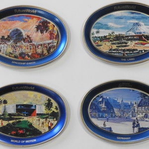 May include: Four oval-shaped blue and gold metal trays with images of different attractions at Epcot, a theme park at Walt Disney World. The trays feature the text "FutureWorld" and the names of the attractions: "Spaceship Earth", "The Land", "World of Motion", and "Germany".