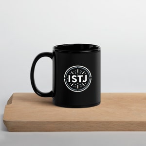 Puede incluir: Taza de cerámica negra con un círculo blanco y el texto "ISTJ" en su interior. El círculo tiene un diseño gris con líneas y puntos.