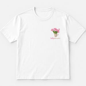 Può includere: Una t-shirt bianca a maniche corte con una piccola grafica sul lato sinistro del petto. La grafica raffigura un bouquet di tulipani rosa in una tazza marrone chiaro con un'icona a forma di cuore, accompagnata dal testo tulipamami in corsivo rosa.