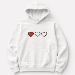 Può includere: Una felpa bianca con cappuccio e maniche lunghe caratterizzata da una grafica con tre cuori pixelati sul petto. Il primo cuore è riempito di rosso, mentre il secondo e il terzo sono bordati di nero con il centro bianco, come una barra della vita.