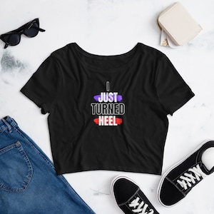 May include: Black cropped t-shirt with the text "I JUST TURNED HEEL" in white with purple and red accents.