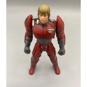Op de afbeelding: Een rood en grijs actiefiguur van een personage met blond haar. De figuur draagt een rood pak met grijze accenten en heeft een vastberaden uitdrukking. De figuur staat rechtop.