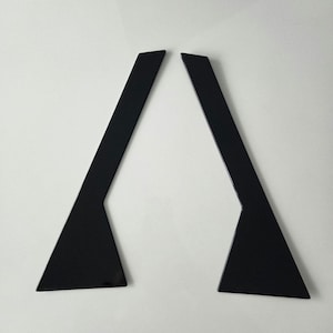 Könnte beinhalten: Zwei schwarze, eckige, geometrische Formen mit dreieckiger Basis und langem, geradem Oberteil. Die Formen sind vor einem weißen Hintergrund platziert, was einen starken Kontrast erzeugt.