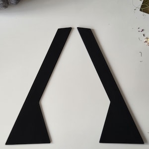 May include: Two identical matte black flat components, each featuring a long, narrow rectangular upper section that transitions into a wider, triangular base. These two pieces are positioned symmetrically to form an inverted V-shape.