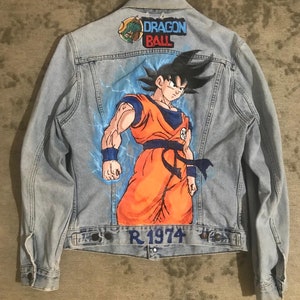 May include: A light blue denim jacket with a hand-painted image of Goku from Dragon Ball Z on the back. The jacket has a patch that says "Dragon Ball" and the text "R 1974" on the bottom.