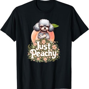 Peut inclure: T-shirt noir avec un caniche blanc portant un collier noir et assis sur une pêche. Le chien est entouré de fleurs roses et blanches. Le texte "Just Peachy" est écrit dans une police rétro.