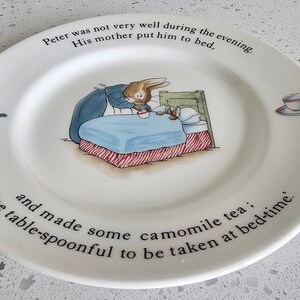 May include: White ceramic plate with a children's illustration of a rabbit in bed, with text around the rim. The plate features a teapot and teacup illustration. The text reads: "Peter was not very well during the evening. His mother put him to bed."