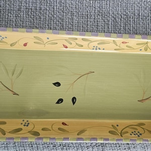 May include: Rectangular ceramic serving platter with a light green center and a decorative border. The border features a yellow band with olive branch designs and a purple and white checkered edge. Olive and leaf motifs are painted on the platter.