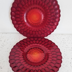 Puede incluir: Dos platos de vidrio rojo rubí con un patrón texturizado similar a burbujas. Los platos tienen un borde festoneado y un centro naranja vibrante. Estos platos decorativos son adecuados para servir o exhibir.