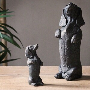 May include: Two black dachshund dog figurines, one standing tall and looking up, the other smaller and looking forward.