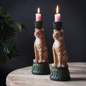 May include: Two tiger-shaped candle holders with green leaves and pink candles. The candle holders are made of ceramic and have a detailed tiger design.