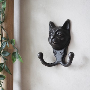 May include: Black cast iron cat head wall hook with two hooks. The cat has a black nose and black eyes.