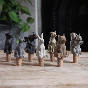 May include: Set of eight animal bottle stoppers. The stoppers are made of a gray, brown, and gold colored resin. The animals include a rabbit, a squirrel, a bear, a leopard, an elephant, a cat, and a dog.