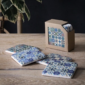 May include: Set of four blue and white ceramic coasters with a geometric pattern. The coasters are in a cardboard box with a window showing the design.