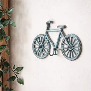 May include: A light blue metal bicycle wall hook. The bicycle is in a vintage style with a curved handlebar and spoked wheels.