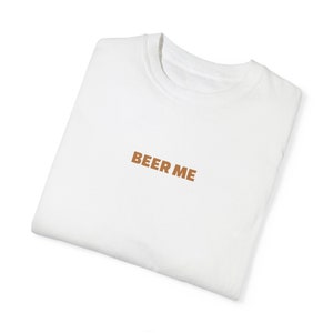 Può includere: Maglietta bianca con la scritta "BEER ME" stampata in marrone sul davanti.