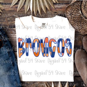 Könnte beinhalten: Weißes T-Shirt mit dem Wort "BRONCOS" in großen, farbenfrohen Buchstaben. Die Buchstaben haben ein Patchwork-Design in Blau und Orange mit blauem Rand. Das Shirt ist von der Marke Comfort Colors.
