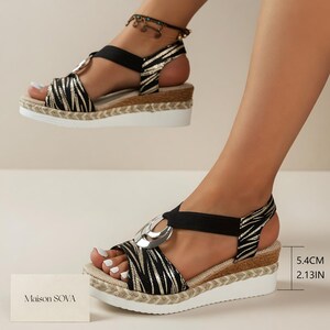 May include: Wedge sandals with a black and gold zebra print design. The sandals have a black elastic strap and a silver ring detail. The platform measures 2.13 inches (5.4 cm) high, with a white sole and a woven jute trim.