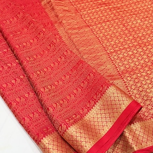 May include: A vibrant red fabric featuring intricate gold metallic thread woven into a repeating geometric pattern across the main body, complemented by a wide border displaying detailed floral and lattice motifs in matching gold thread.