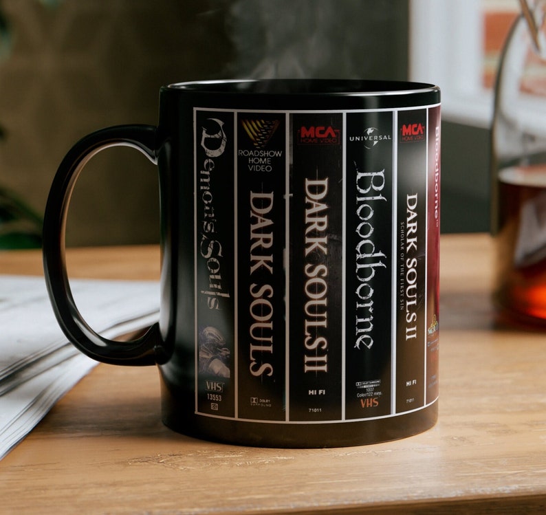 This is a retro style from software dark souls mug, the design wraps around the mug, in the design you can see spines of the from software  games with vhs details. The mug is black.