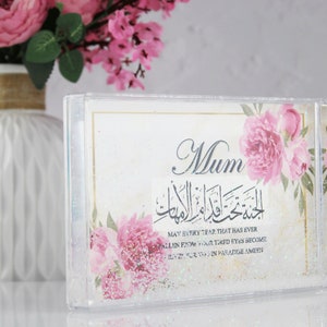 May include: A clear acrylic frame with a white background and pink floral design. The frame has a quote in Arabic script and English text that reads "May every tear that has ever fallen from your tired eyes become a river flowing in paradise, Ameen." The frame also has the word "Mum" in large, black letters.