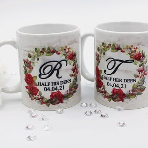 Pode incluir: Duas canecas de cerâmica branca com desenhos florais e as letras "R" e "T" em uma coroa. As canecas têm o texto "Half his Deen 04.04.21" e "Half her Deen 04.04.21".
