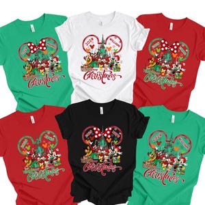 Könnte beinhalten: Fünf T-Shirts in Grün, Weiß, Rot und Schwarz mit einer Grafik von Disney-Figuren vor einem Schloss, einer Mickey-Maus-Ohren-Kontur, dem Jahr 2026, personalisierten Namen und dem Text Very Merry Christmas in roter Schreibschrift.