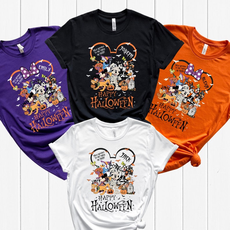 May include: Four t-shirts in purple, black, white, and orange, each featuring a Halloween-themed graphic. The design includes Disney characters dressed in costumes, the text "Happy Halloween," and personalized names within Mickey Mouse ears.