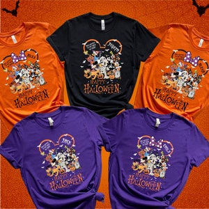 May include: A collection of Halloween-themed t-shirts in orange, black, and purple. Each shirt features a graphic of Disney characters dressed in Halloween costumes, with the words "Happy Halloween" and a name printed on the design. The shirts are short-sleeved.