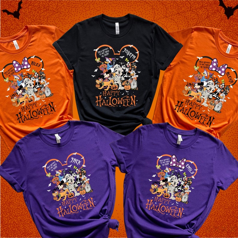 May include: A collection of Halloween-themed t-shirts in orange, black, and purple. Each shirt features a graphic of Disney characters dressed in Halloween costumes, with the words "Happy Halloween" and a name printed on the design. The shirts are short-sleeved.