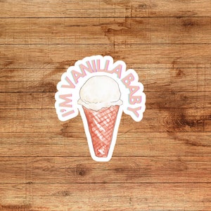 Op de afbeelding: Een witte ijshoorn met de tekst "I'm Vanilla Baby" in roze en blauwe letters op een houten achtergrond.