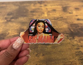 Peut inclure: Un autocollant représentant une femme aux longs cheveux noirs, portant un haut jaune et un collier argenté. L'autocollant porte le texte "BIG MAMA" en lettres roses.