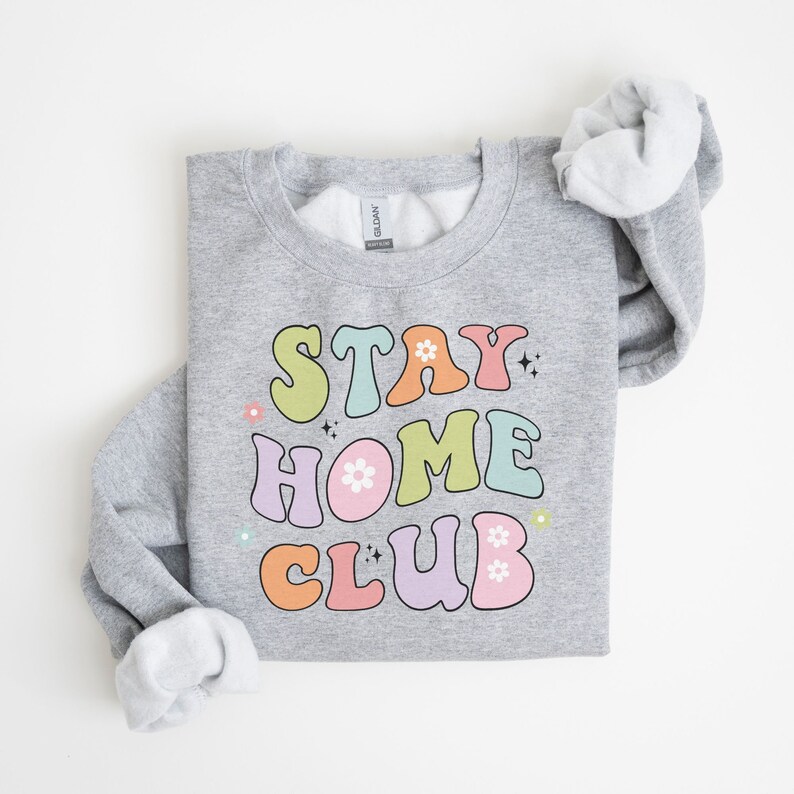 May include: A gray sweatshirt with the text "STAY HOME CLUB" in colorful retro-style lettering with flowers and sparkles.