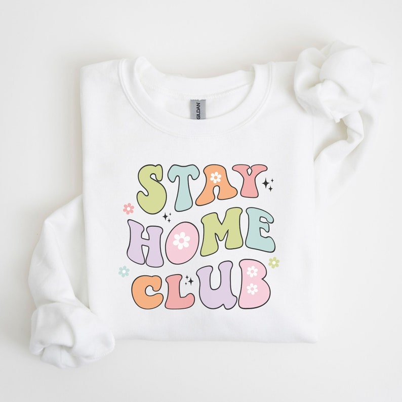 May include: White sweatshirt with a colorful retro-style graphic that says "Stay Home Club" with flowers and sparkles.