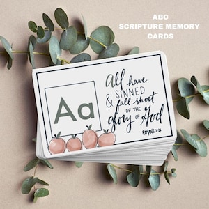 Puede incluir: Una tarjeta blanca con la letra "Aa" en un cuadro gris. La tarjeta tiene un versículo de la Biblia: "Porque todos pecaron y están destituidos de la gloria de Dios." Romanos 3:23. La tarjeta está decorada con manzanas rosas.