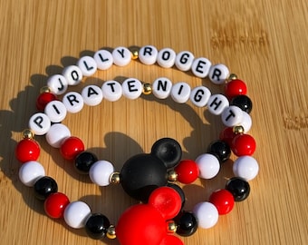 May include: Two beaded bracelets with black, white, and red beads. One bracelet spells "Jolly Roger" and the other spells "Pirate Night". The bracelets have Mickey Mouse charms.