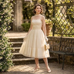 May include: A cream-colored midi dress with thin spaghetti straps, a gathered bodice, and a full skirt. The dress is paired with a multi-strand pearl necklace, short white gloves, a small gold-toned rectangular handbag, and cream-colored pumps.