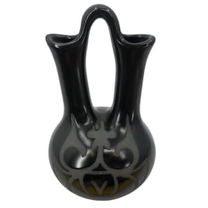 May include: A black ceramic vase with a unique double-spout design and a handle arching over the top. The vase features a decorative gray tribal pattern on the rounded base. The glossy finish enhances the dark color, creating a striking contrast.